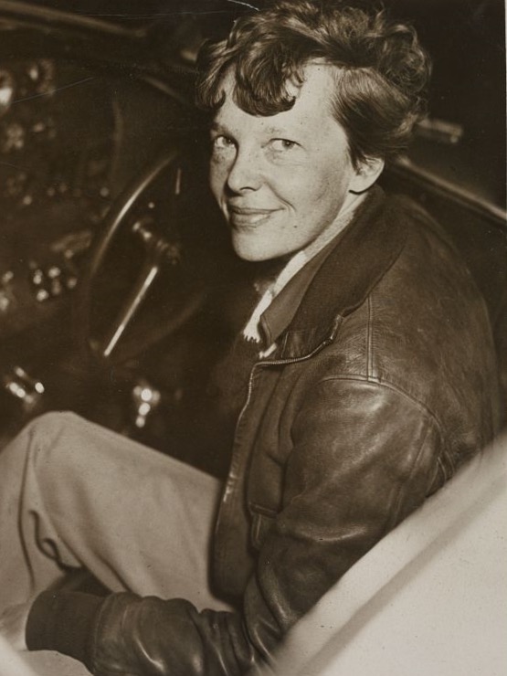 Amelia Earhart in 1937, smiling in the cockpit of her Lockheed Electra, in a brown leather flying jacket
