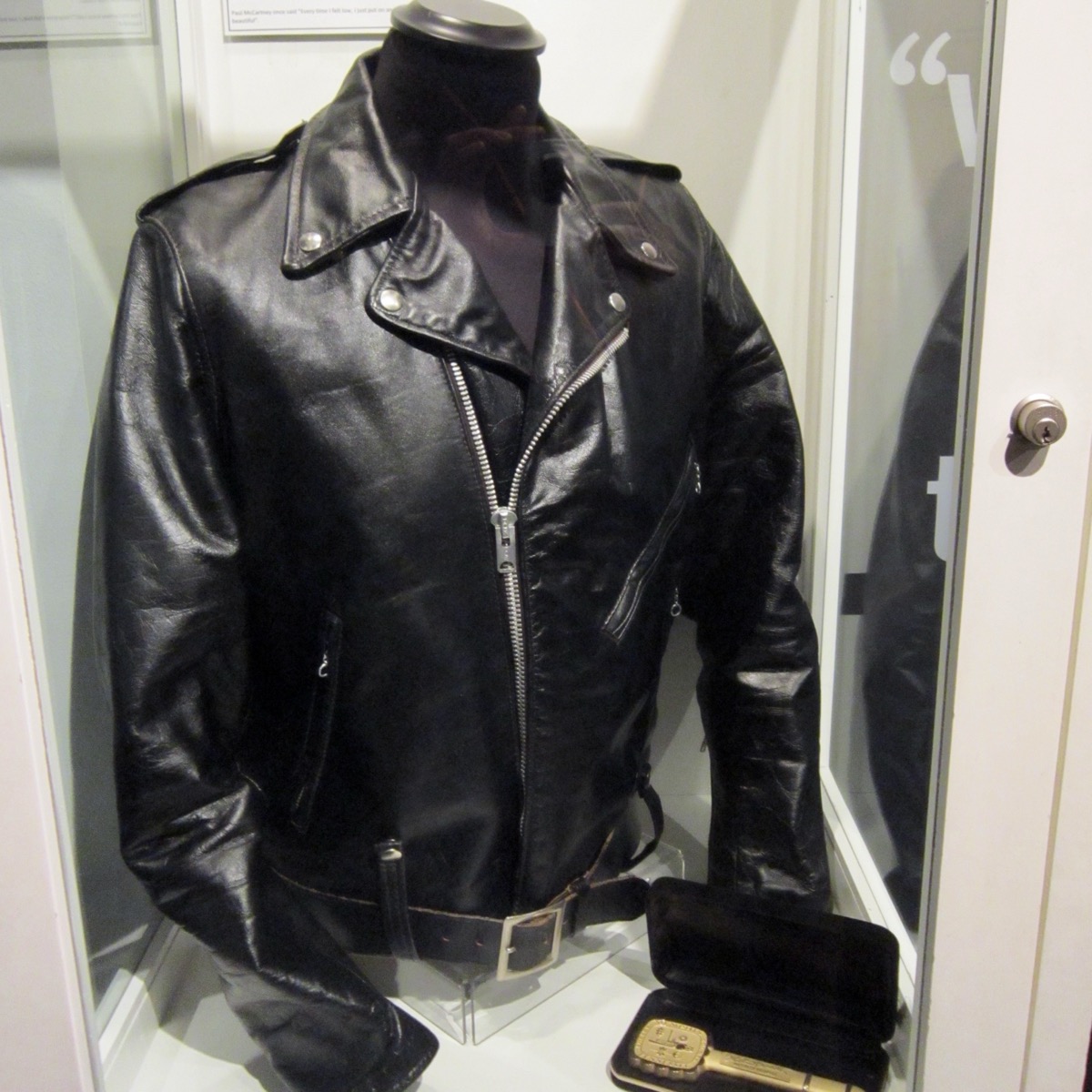 Elvis Presley's black leather motorcycle jacket with an off-centre zip and a belt, in a museum display case