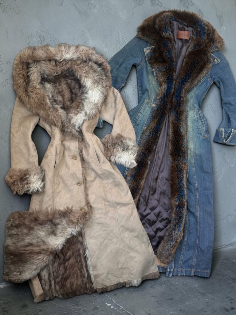 A long beige suede coat with a shaggy fur hood and cuffs beside a long denim coat lined with shaggy faux fur