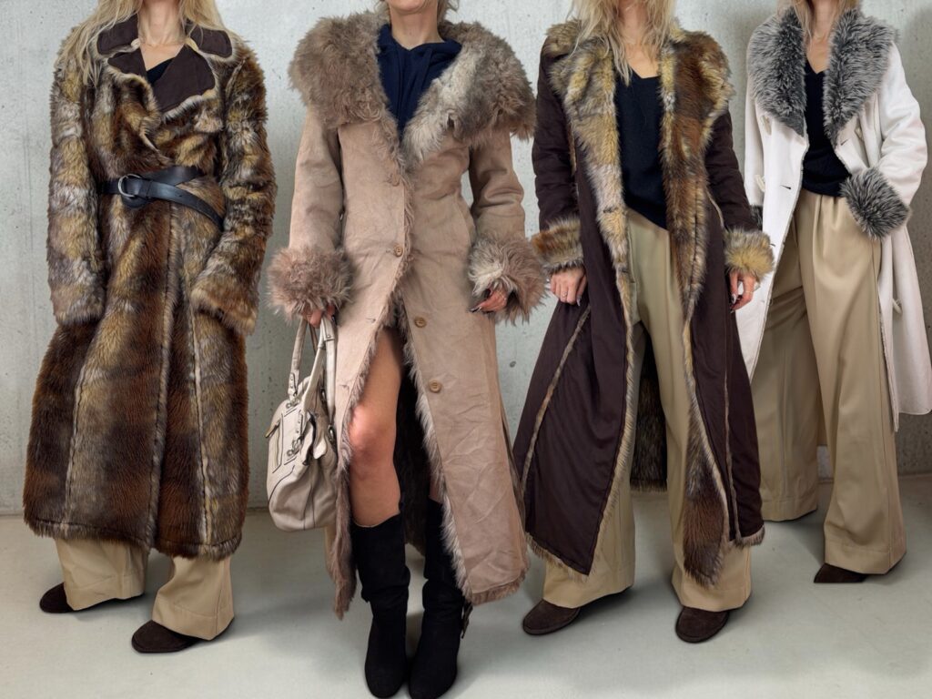 Four long shaggy coats worn with wide trousers: a faux fur maxi coat, a beige suede Penny Lane coat, a dark brown coat with fur trim and a white coat with a grey fur collar