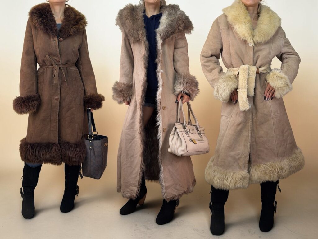 Three Penny Lane coats worn from the front: brown suede with fur trim and a tie belt, a long beige coat with a shaggy collar, and a cream shearling with a belt