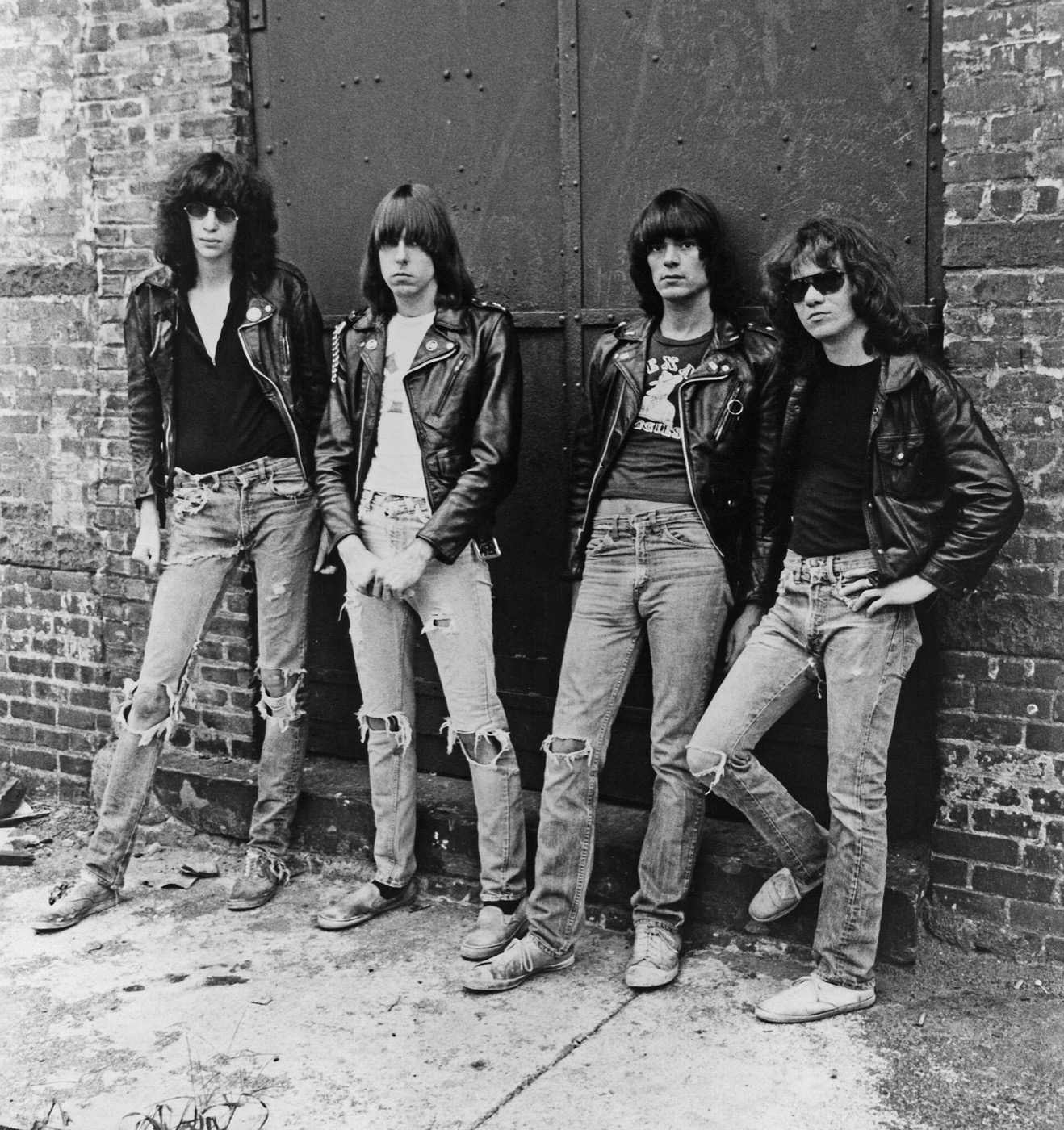 The four Ramones in 1977 standing against a brick wall in black leather biker jackets, T-shirts and ripped jeans