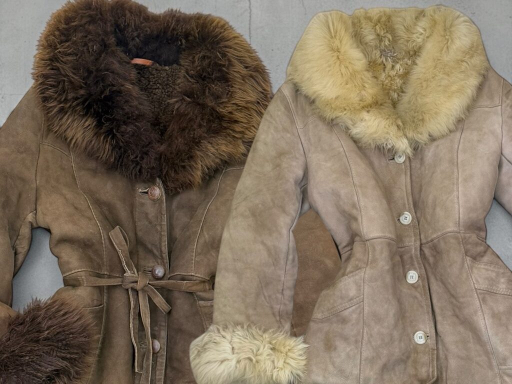 Close-up of two sheepskin coat collars, one dark brown and one cream, above tan and grey suede with buttons and a tie belt