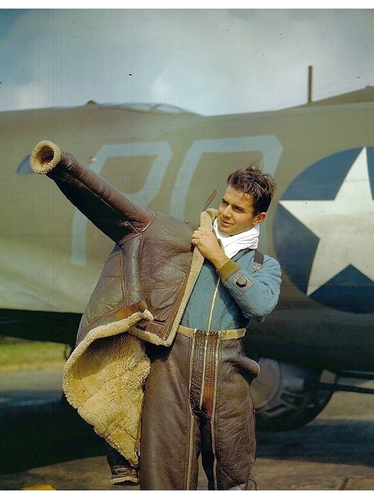 A US air gunner in 1943 putting on a brown sheepskin flying jacket with a thick fleece lining, in front of a B-17 bomber