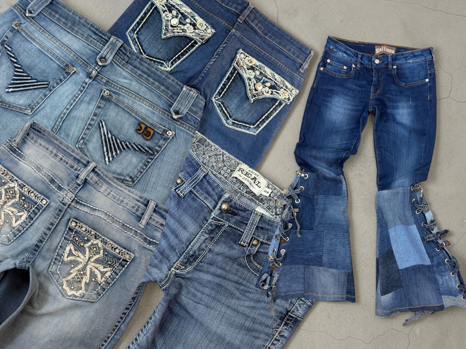 Original 2000s low rise jeans laid out with embroidered back pockets, beside a pair of patchwork flares laced up the leg